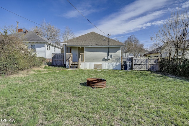 back of property featuring roof with shingles, a yard, a gate, fence, and a fire pit