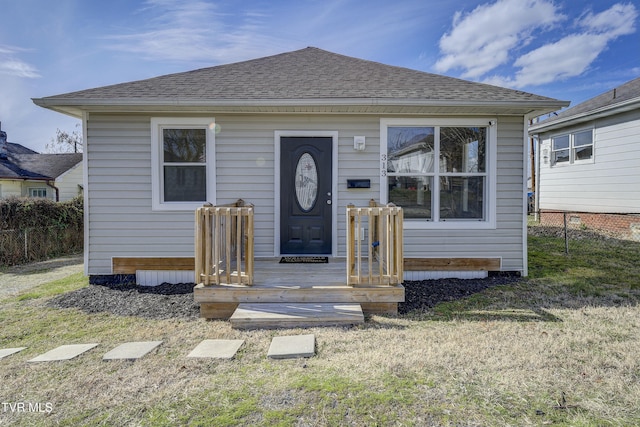 bungalow with roof with shingles, a front yard, and fence