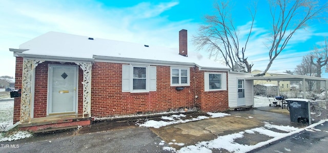 view of front of home with an attached carport, brick siding, and a chimney