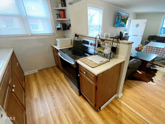 kitchen featuring light countertops, light wood-style floors, stainless steel electric range, and brown cabinets