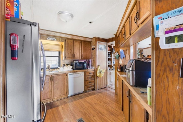 kitchen with brown cabinetry, freestanding refrigerator, light wood-type flooring, black microwave, and dishwasher