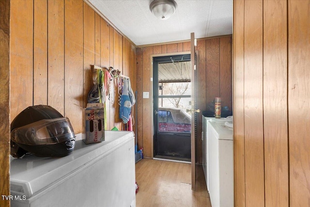 washroom with light wood-type flooring, laundry area, washing machine and dryer, and wooden walls