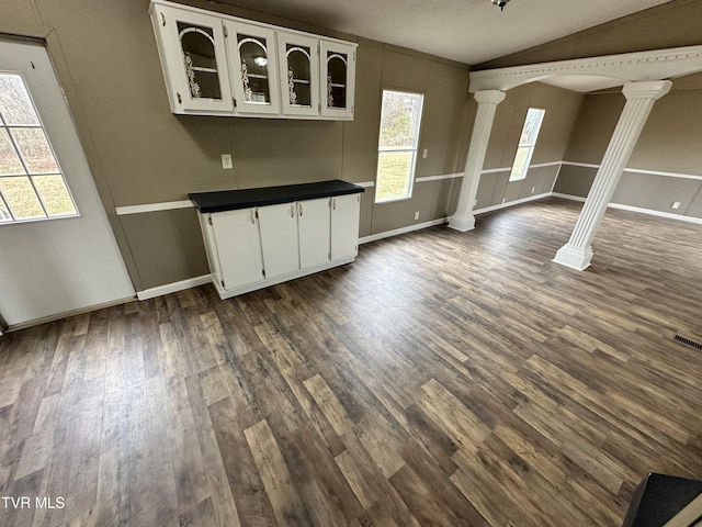 unfurnished dining area with lofted ceiling, baseboards, dark wood finished floors, and ornate columns