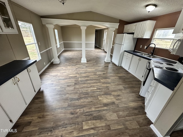 kitchen with decorative columns, dark countertops, freestanding refrigerator, vaulted ceiling, and a sink