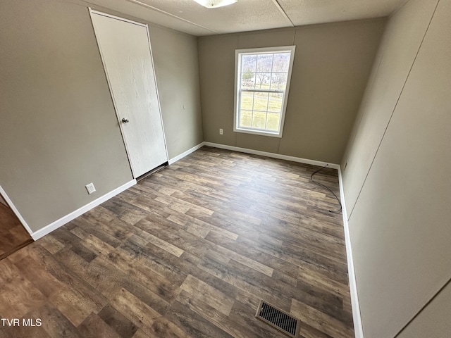 unfurnished room featuring visible vents, dark wood finished floors, and baseboards