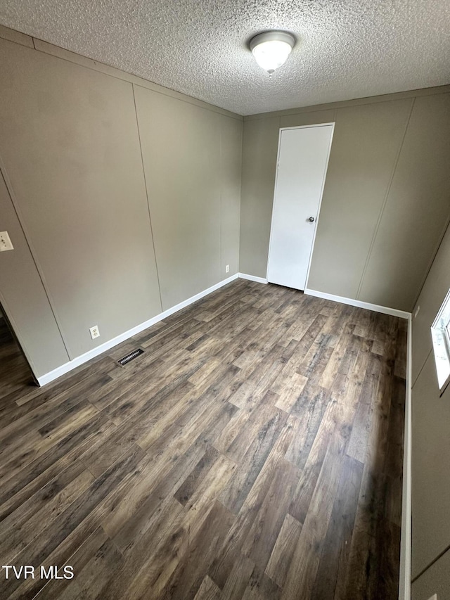 unfurnished bedroom featuring a textured ceiling, dark wood finished floors, visible vents, and baseboards