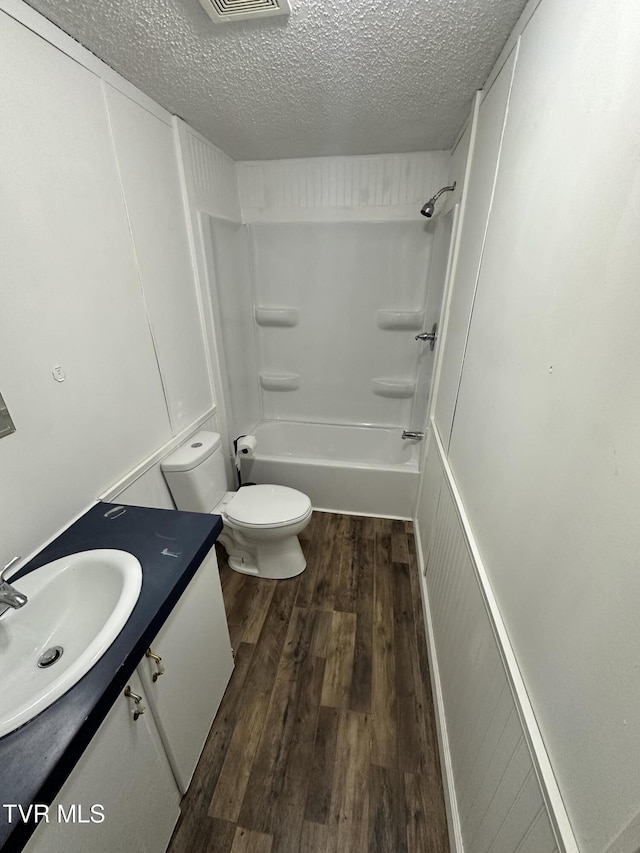 full bathroom with bathing tub / shower combination, toilet, wood finished floors, a textured ceiling, and vanity