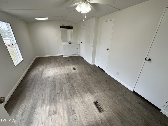 unfurnished bedroom featuring lofted ceiling, a sink, visible vents, baseboards, and dark wood-style floors