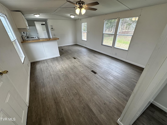 unfurnished living room with visible vents, a ceiling fan, vaulted ceiling, baseboards, and dark wood-style floors