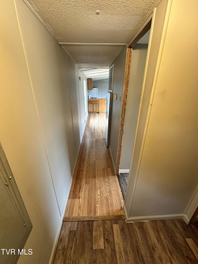 hallway featuring a textured ceiling, baseboards, and wood finished floors