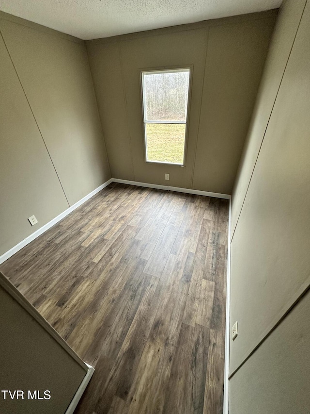 unfurnished room featuring a textured ceiling, baseboards, and wood finished floors