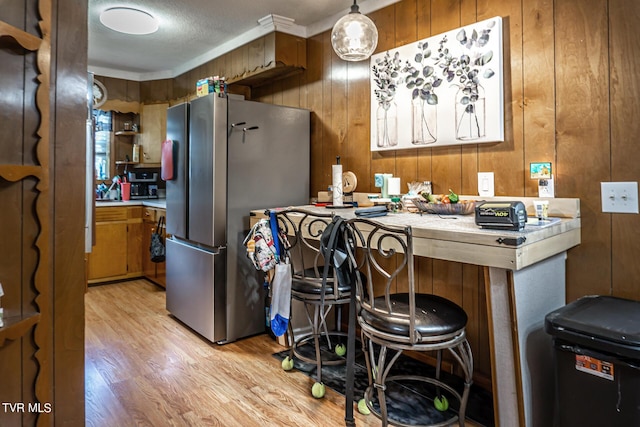 kitchen with wood walls, light wood-style floors, light countertops, freestanding refrigerator, and brown cabinets