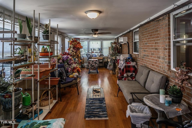 living area with ceiling fan, hardwood / wood-style floors, and brick wall
