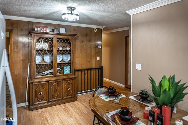 dining area with a textured ceiling, ornamental molding, light wood-style flooring, and wooden walls