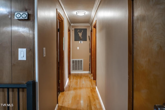 corridor with light wood-style floors, baseboards, visible vents, and ornamental molding
