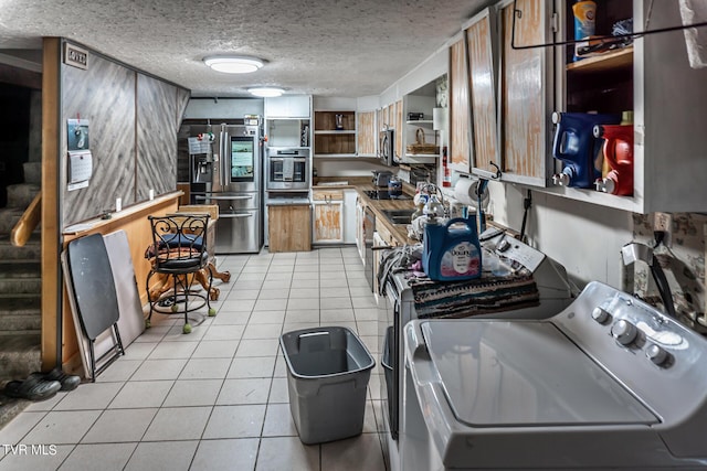 kitchen featuring light tile patterned floors, a textured ceiling, stainless steel appliances, open shelves, and washer and clothes dryer