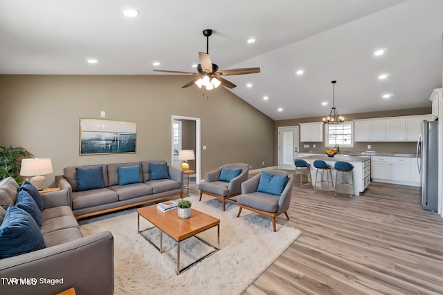 living area featuring light wood-style floors, lofted ceiling, ceiling fan with notable chandelier, and recessed lighting