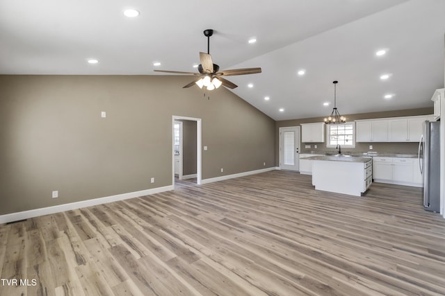 kitchen featuring open floor plan, vaulted ceiling, freestanding refrigerator, a center island, and light wood finished floors