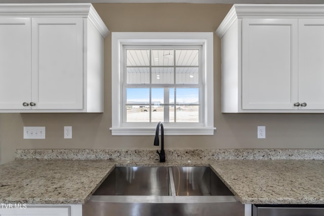 kitchen featuring light stone countertops, white cabinetry, and a sink