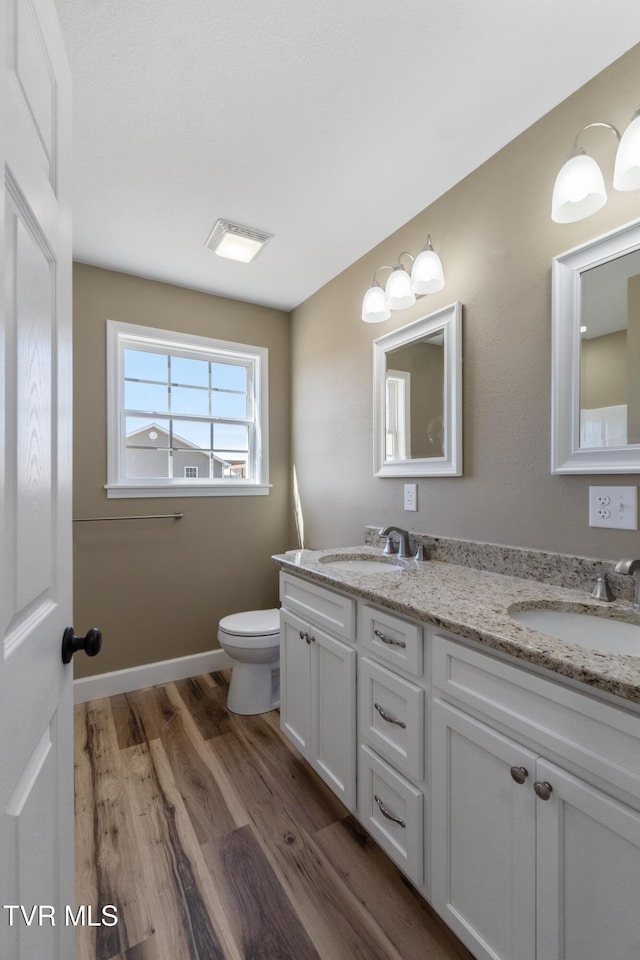 bathroom with double vanity, a sink, toilet, and wood finished floors