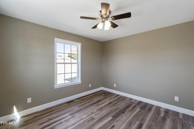 spare room with a ceiling fan, visible vents, baseboards, and wood finished floors