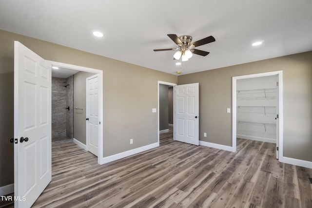 unfurnished bedroom with recessed lighting, a spacious closet, baseboards, and wood finished floors