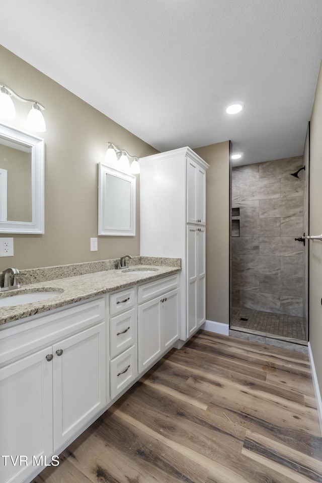 full bath with double vanity, a tile shower, a sink, and wood finished floors