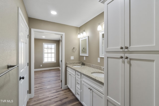 full bathroom with double vanity, a sink, baseboards, and wood finished floors