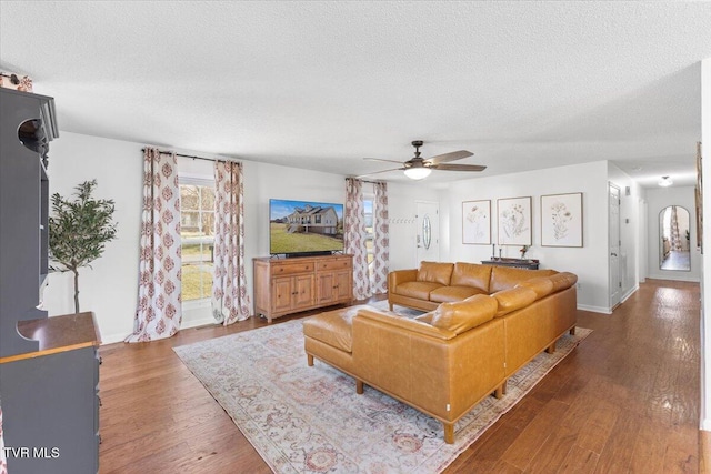 living area with ceiling fan, a textured ceiling, baseboards, and wood finished floors