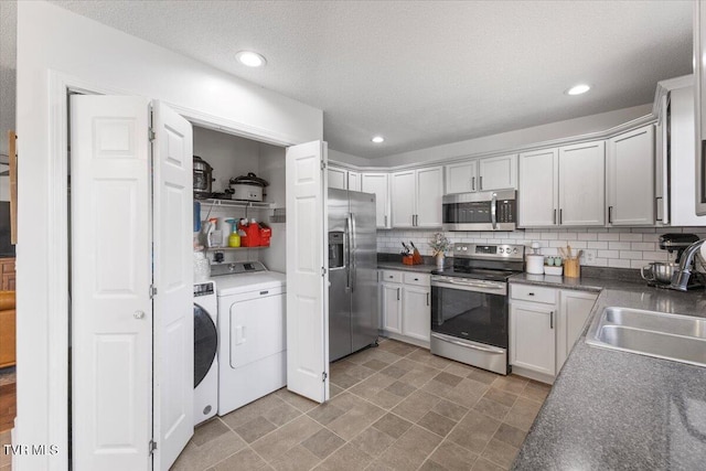 kitchen with washing machine and clothes dryer, stainless steel appliances, dark countertops, decorative backsplash, and a sink