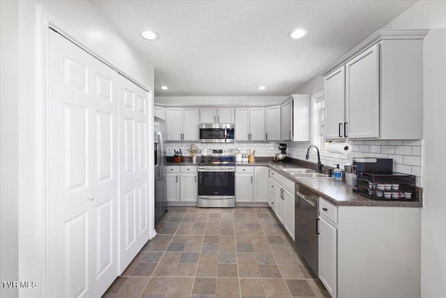 kitchen with appliances with stainless steel finishes, dark countertops, a sink, and decorative backsplash