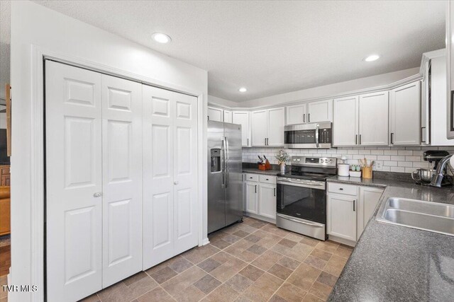 kitchen with dark countertops, appliances with stainless steel finishes, a sink, stone finish flooring, and backsplash