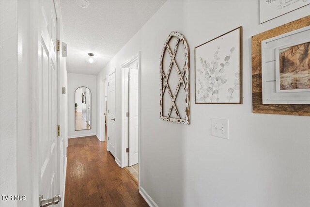 corridor with a textured ceiling, baseboards, and wood finished floors