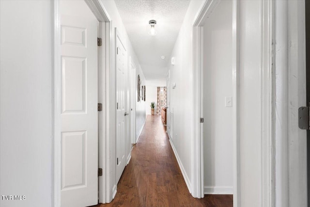 hallway featuring a textured ceiling, baseboards, and wood finished floors