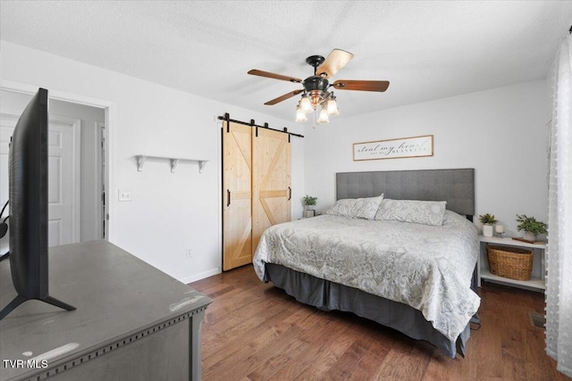 bedroom featuring wood finished floors, ceiling fan, a textured ceiling, and a barn door