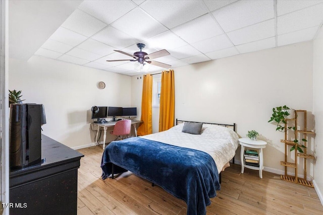 bedroom with ceiling fan, a drop ceiling, wood finished floors, and baseboards