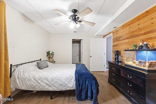 bedroom with a ceiling fan, wooden walls, and wood finished floors