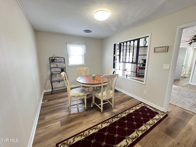 dining area with a textured ceiling, baseboards, and wood finished floors