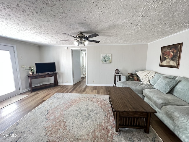 living area with a textured ceiling, ornamental molding, wood finished floors, and a ceiling fan