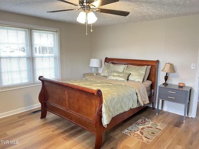 bedroom with a textured ceiling, ceiling fan, wood finished floors, visible vents, and baseboards