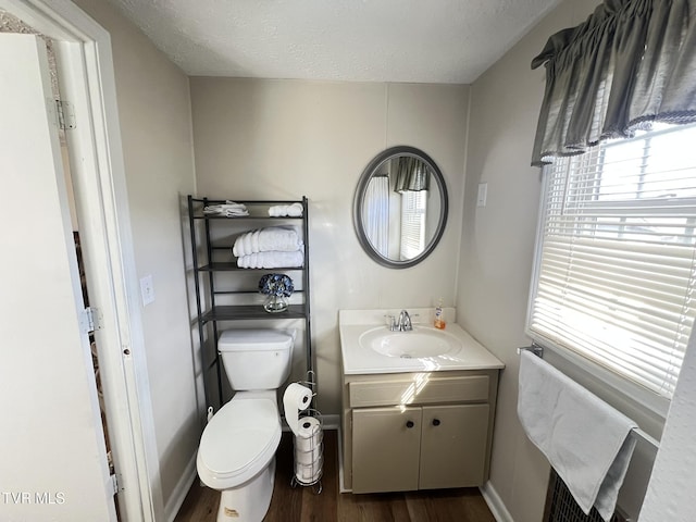 bathroom with toilet, a textured ceiling, vanity, wood finished floors, and baseboards