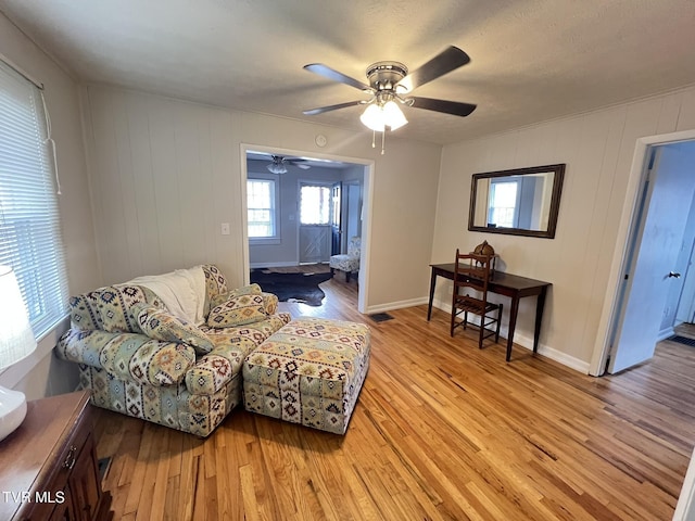 living area with light wood finished floors, a ceiling fan, and baseboards