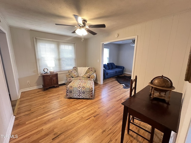 living area featuring baseboards, ceiling fan, a textured ceiling, and light wood finished floors