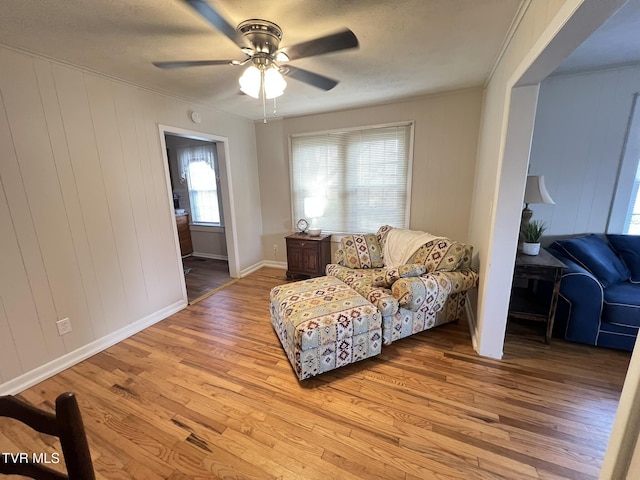 sitting room with light wood-style floors, baseboards, ornamental molding, and a ceiling fan