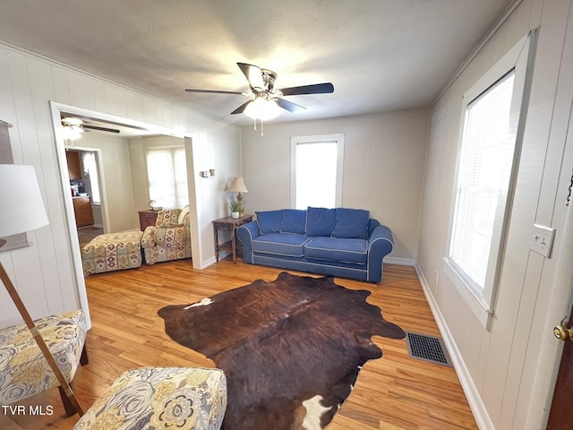 living area with baseboards, ceiling fan, visible vents, and wood finished floors