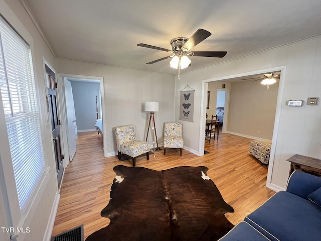 living room with ceiling fan, light wood-style flooring, visible vents, baseboards, and ornamental molding