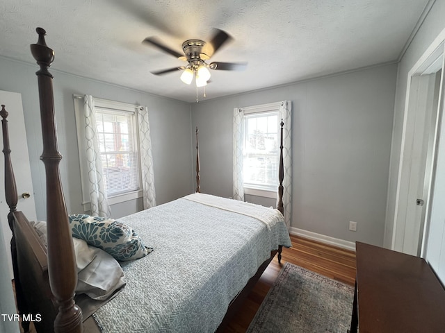 bedroom with a ceiling fan, a textured ceiling, baseboards, and dark wood-style flooring