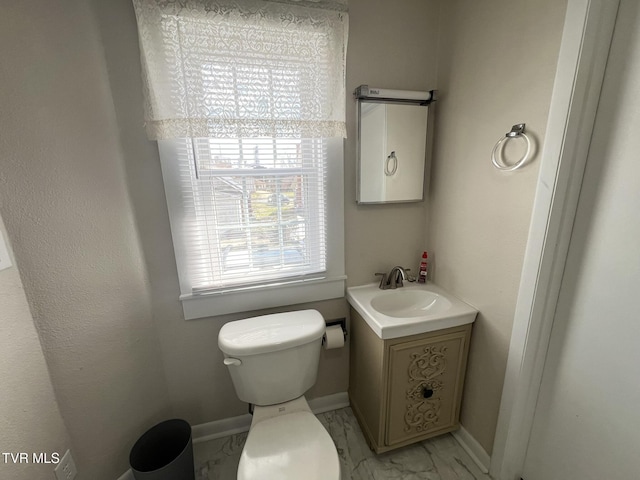 half bath featuring toilet, marble finish floor, vanity, and baseboards