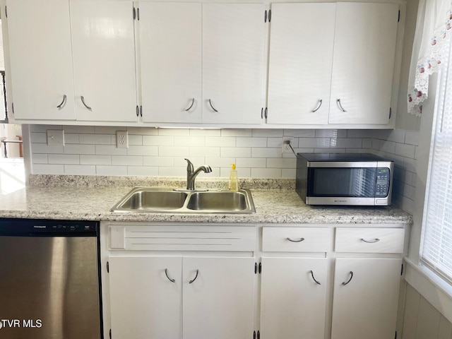 kitchen with appliances with stainless steel finishes, a sink, white cabinetry, and decorative backsplash