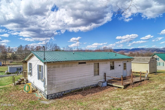 back of property featuring metal roof, crawl space, a storage unit, a deck, and an outdoor structure